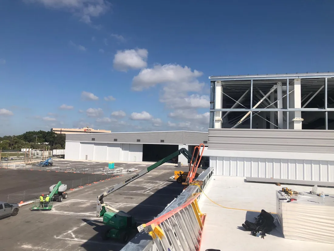 Icon Roofing crew installing a white flat membrane roof on a commercial building with aerial lifts