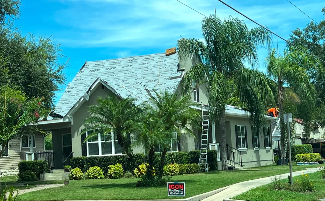 Roof replacement in progress with new underlayment and an Icon Roofing yard sign